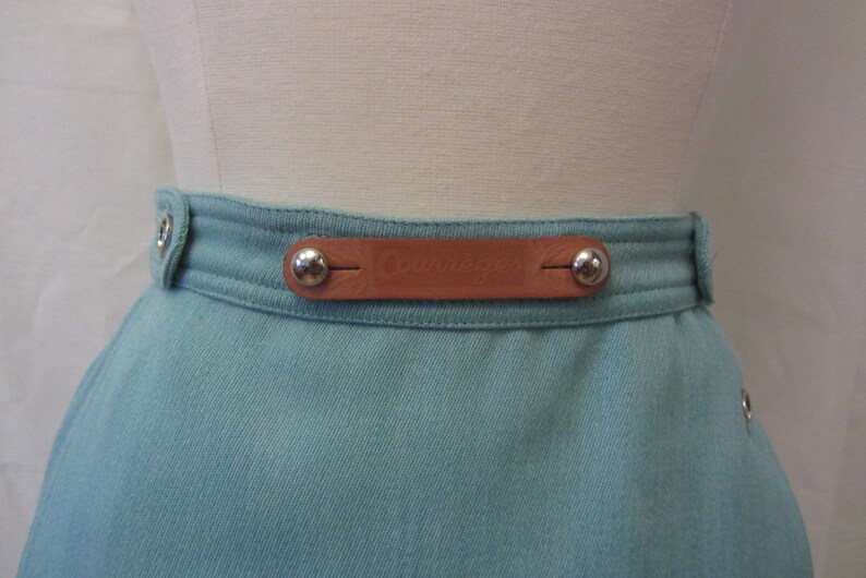 May include: A light blue skirt with a brown leather belt and silver metal buckles. The belt has the word "Couturier" embossed on it.