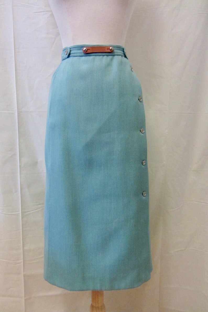 May include: A light blue skirt with a brown leather belt and silver buttons down the side.