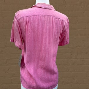 May include: A pink short-sleeved button-down shirt with a collar. The shirt is made of a lightweight fabric and has a relaxed fit.