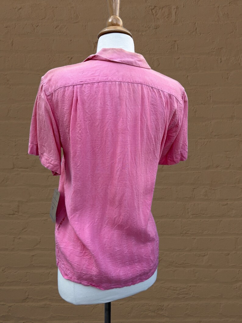 May include: A pink short-sleeved button-down shirt with a collar. The shirt is made of a lightweight fabric and has a relaxed fit.