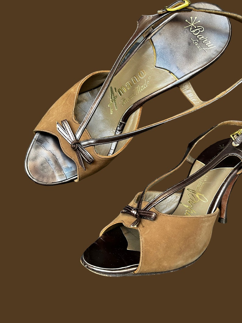 K&ouml;nnte beinhalten: Ein Paar braune Wildledersandalen mit Absatz, Peeptoe und Schleife. Die Sandalen haben eine goldene Schnalle und sind mit "A'mano Hand Made" und "Barry Stuart" beschriftet.