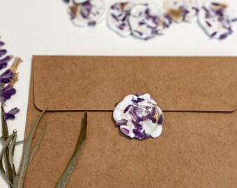 Peut inclure: Une enveloppe en papier kraft avec un sceau de cire violet et blanc. L'enveloppe est sur une surface blanche avec une brindille de lavande.