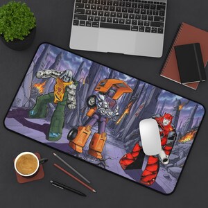 May include: A rectangular mousepad featuring a comic book style illustration of three robots in a futuristic setting. The robots are in shades of orange, green, purple, and red. A computer mouse sits on the mousepad.
