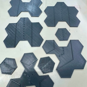May include: A set of 10 gray 3D printed hexagonal tiles with various shapes and sizes. The tiles have a textured surface and are designed to be used together to create a unique pattern.