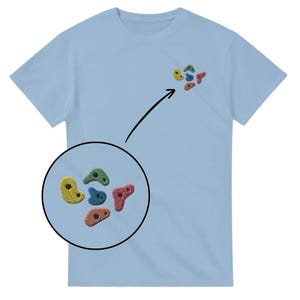 Può includere: T-shirt azzurra con un piccolo disegno ricamato di prese d'arrampicata colorate. Il disegno comprende forme gialle, verdi, blu e rosso-arancio. La maglietta è realizzata in un tessuto morbido e chiaro.