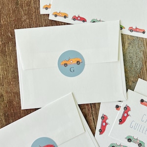 May include: A set of white stationery with a blue and white car design. The stationery includes envelopes and note cards. The note cards have the name "CJ Guillen" printed on them. The envelopes have a blue circle with a yellow car and the letter "G" in the center.