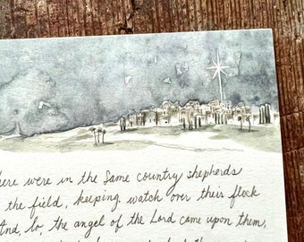May include: A watercolour painting of a night sky with a bright star shining down on a small village. The text below the image reads: "And, lo, the angel of the Lord came upon them, and the glory of the Lord shone round about them: and they were afraid. And the angel said unto them, For, behold, I bring you good tidings of great joy, which shall be to all people. For unto you is born this day in the city of David a Savior, which is Christ the Lord."