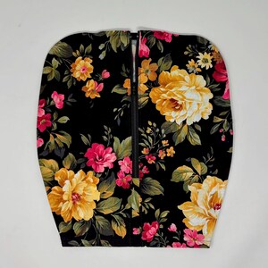 May include: A black fabric panel featuring a vibrant floral pattern with large yellow roses and smaller pink blossoms interspersed with green leaves. A vertical black zipper runs down the center, dividing the fabric into two symmetrical halves.
