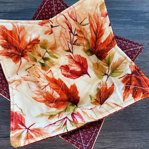 Puede incluir: Dos salvamanteles hechos a mano. El salvamanteles superior presenta un fondo crema con un estampado de hojas de otoño naranjas, rojas y verdes. El salvamanteles inferior es de color burdeos oscuro con un estampado de puntos blancos. Ambos están cosidos.