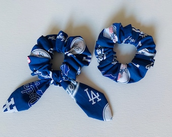 May include: Two blue and white scrunchies with the Los Angeles Dodgers logo. One scrunchie is tied into a bow.