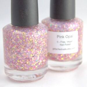 May include: Two bottles of pink glitter nail polish with a label that reads "Pink Opal 5-Free, Vegan Nail Polish glitterfiednails.etsy.com"