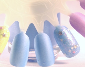 Op de afbeelding: Een set van vijf nagellakken in verschillende tinten blauw en paars. De lakken worden gepresenteerd op een witte kunststof nagellakhouder. Een van de lakken heeft blauwe glitter met witte sterren.
