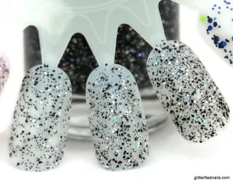 May include: Close-up of four nail polish bottles with a clear base and black and silver glitter. The bottles are arranged in a row on a white surface.