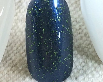 Puede incluir: Un esmalte de uñas azul oscuro con purpurina verde. El esmalte se aplica a una uña.