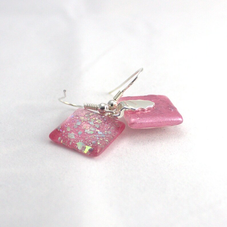 May include: A pair of pink glass earrings with silver hooks. The glass is sparkly and has a light pink color.