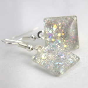 May include: Silver dangle earrings with iridescent glitter encased in clear square glass.