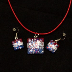 Peut inclure: Un collier et des boucles d'oreilles assortis en paillettes rouge, blanc et bleu. Le collier a un pendentif carr&eacute; avec des paillettes rouge, blanc et bleu et des &eacute;toiles. Les boucles d'oreilles sont &eacute;galement carr&eacute;es et ont des paillettes rouge, blanc et bleu et des &eacute;toiles.
