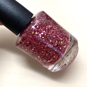 May include: A clear glass bottle of pink glitter nail polish with a black cap.