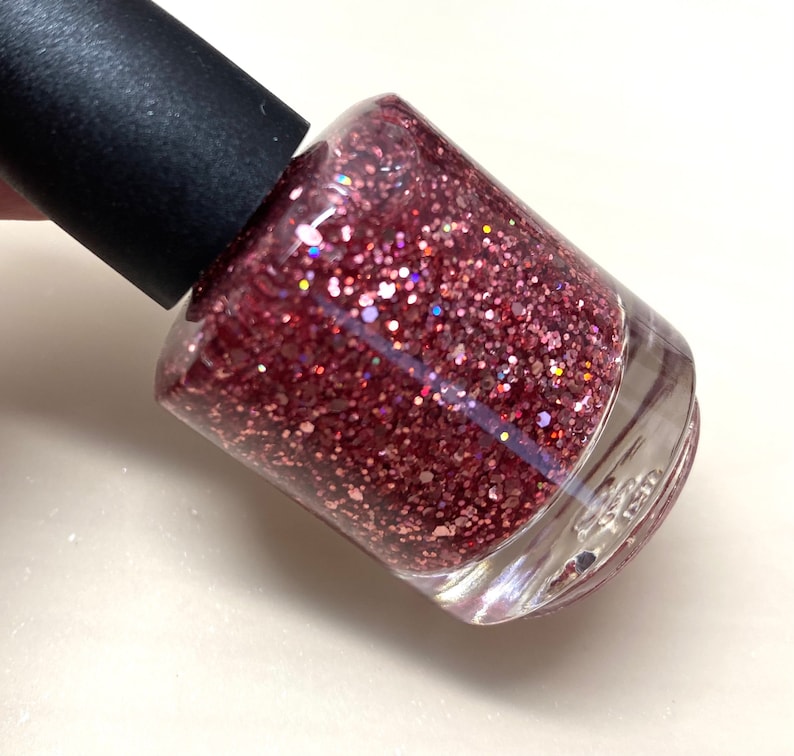 May include: A clear glass bottle of pink glitter nail polish with a black cap.