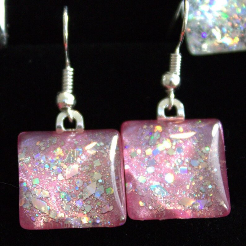 May include: A pair of silver dangle earrings with square pink glitter resin charms.