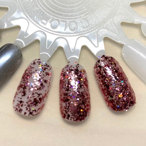 May include: Three nail polish swatches on a white color wheel. The swatches are a shimmery pink with red glitter.