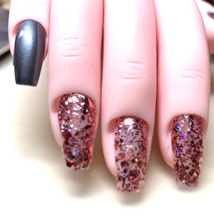 May include: Close-up of four fingernails with nail polish. One nail is painted a metallic silver color, and the other three are painted with a rose gold glitter polish.