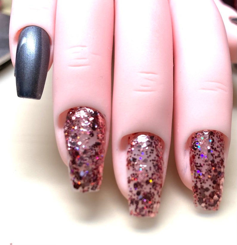 May include: Close-up of four fingernails with nail polish. One nail is painted a metallic silver color, and the other three are painted with a rose gold glitter polish.