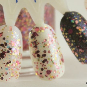 May include: Close-up of five nail polish bottles with different colored glitter finishes. The bottles are arranged in a row on a white surface. The glitter colors include pink, gold, black, and white.