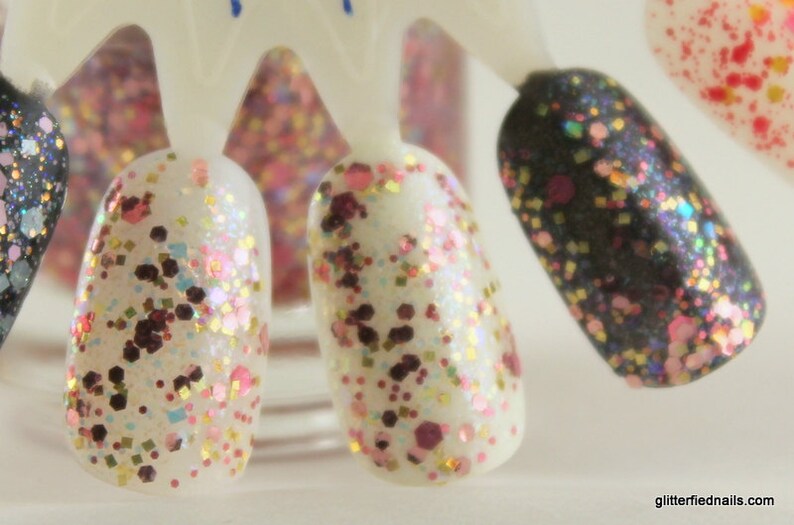 May include: Close-up of five nail polish bottles with different colored glitter finishes. The bottles are arranged in a row on a white surface. The glitter colors include pink, gold, black, and white.