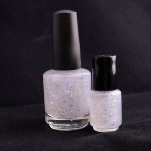 May include: Two bottles of clear nail polish with a white iridescent glitter finish. The bottles have black caps.