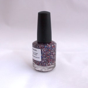 Peut inclure: Un flacon de vernis &agrave; ongles paillet&eacute; rouge, blanc et bleu transparent avec un bouchon noir. Le flacon porte une &eacute;tiquette indiquant "Patriotic 3-Free, Vegan Nail Polish" et une adresse de site Web.