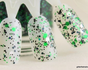 May include: Close-up of three fingernails painted with a clear base coat and green and black glitter.