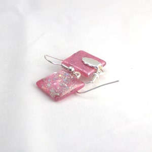May include: Pink square glass earrings with silver glitter and a silver charm.
