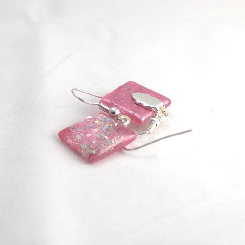 May include: Pink square glass earrings with silver glitter and a silver charm.