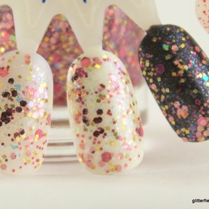 May include: Close-up of five different nail polishes with glitter. The polishes are in a variety of colors, including white, black, and pink. The glitter is in different sizes and shapes.