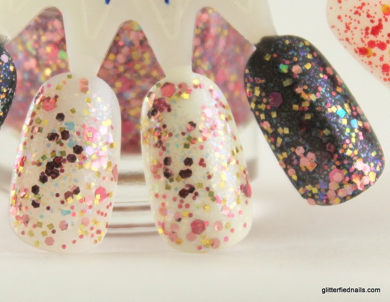 May include: Close-up of five different nail polishes with glitter. The polishes are in a variety of colors, including white, black, and pink. The glitter is in different sizes and shapes.