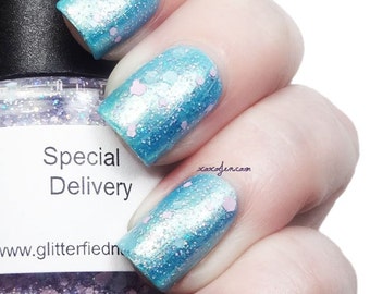 May include: A bottle of light blue nail polish with a shimmery finish and pink glitter. The bottle is labeled "Special Delivery" and "www.glitterfiednails.com".