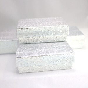 May include: Three silver gift boxes stacked on top of each other. The boxes have a textured, cracked finish.