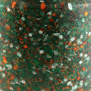 May include: A close-up of a green nail polish bottle with orange and white glitter.