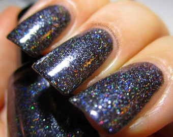May include: Close-up of three fingernails painted with a dark blue nail polish with iridescent glitter. The text "THE BEAUTY OF NAIL POLISH" is visible in the background.