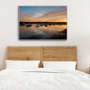May include: A framed photograph of a harbor with boats docked at sunset. The sky is a mix of blue, orange, and pink with clouds. The water is calm and reflects the colors of the sky.