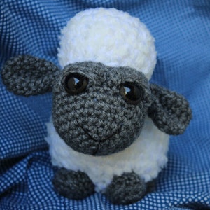 May include: A crocheted stuffed sheep toy with a white fleece body and a gray face. The sheep has large black eyes and a small black nose.
