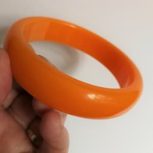 Puede incluir: Un brazalete de plástico naranja brillante. El brazalete es liso y brillante.