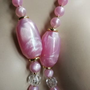 Op de afbeelding: Een roze en witte iriserende kralenketting met gouden accenten. De ketting heeft grote, ovale kralen met een marmerpatroon.