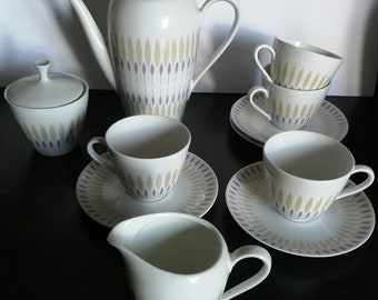 May include: A white tea set with a geometric pattern of green and purple leaves. The set includes a teapot, sugar bowl, creamer, and four cups and saucers.