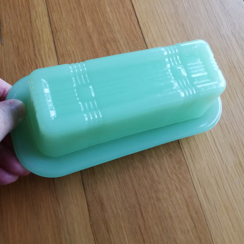 May include: A vintage green glass butter dish with a lid. The dish is rectangular in shape and has a smooth, glossy finish.