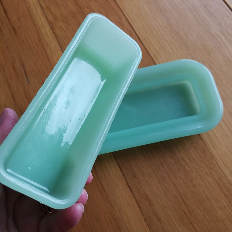 May include: A light green rectangular ceramic dish with a lid. The dish is made of a smooth, glossy material. The lid is slightly raised in the centre.