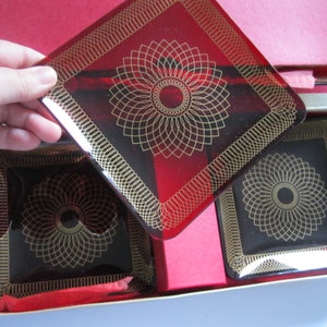 May include: Set of four square glass serving dishes with gold geometric designs on a red and black background. The dishes are in a box with red tissue paper.