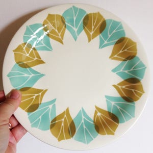 May include: A white ceramic dinner plate with a teal and brown leaf pattern around the rim.