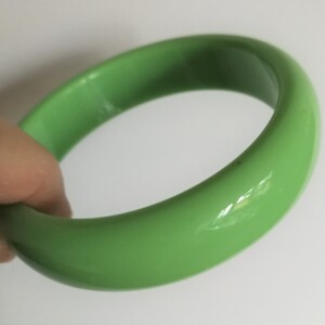Puede incluir: Un brazalete de plástico verde brillante. El brazalete es liso y brillante.